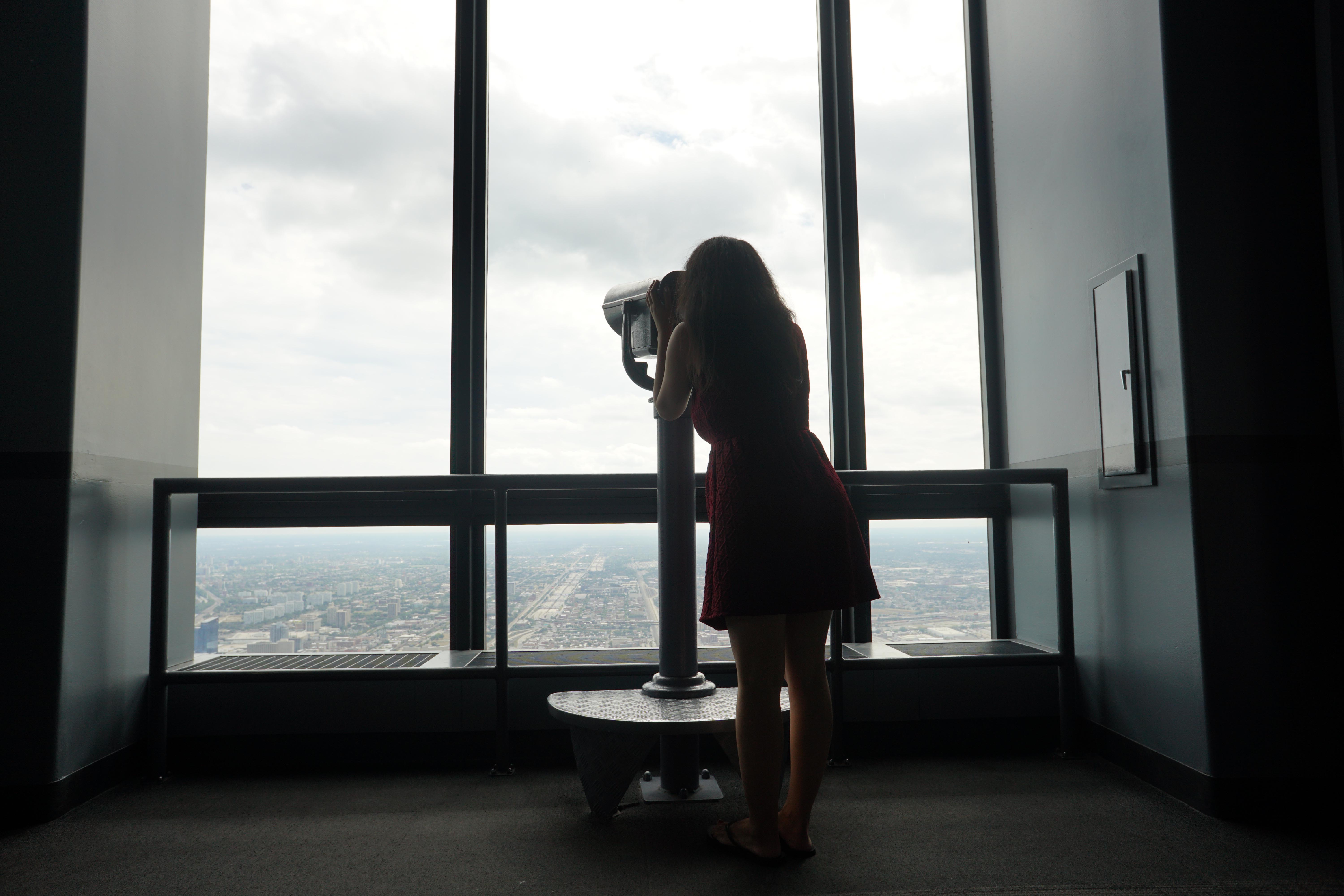 Silhouette of a woman looking through the telescope at Skydeck in Chicago