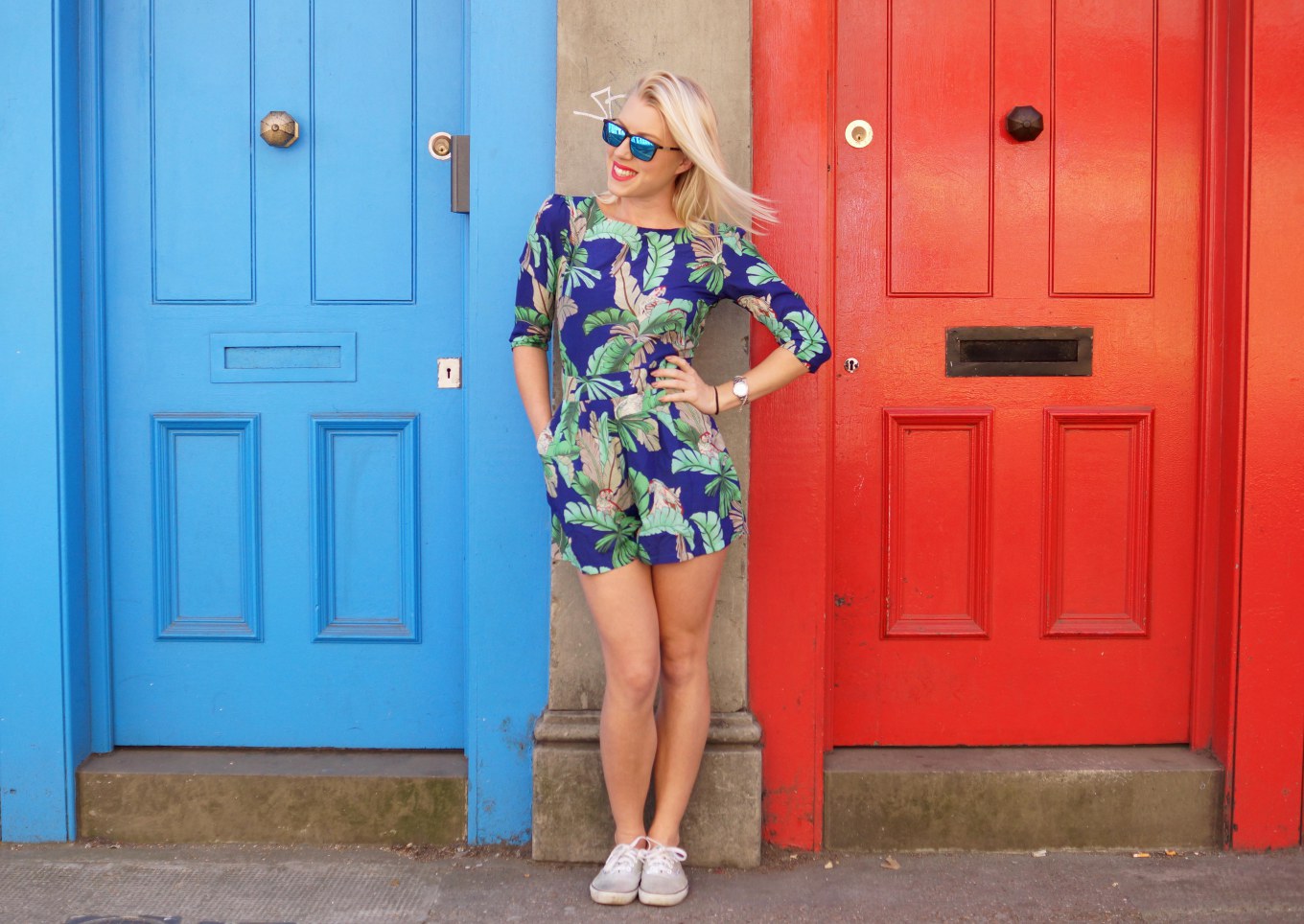 Photo of Louise between a blue and red door wearing a cute thrifted romper with floral pattern