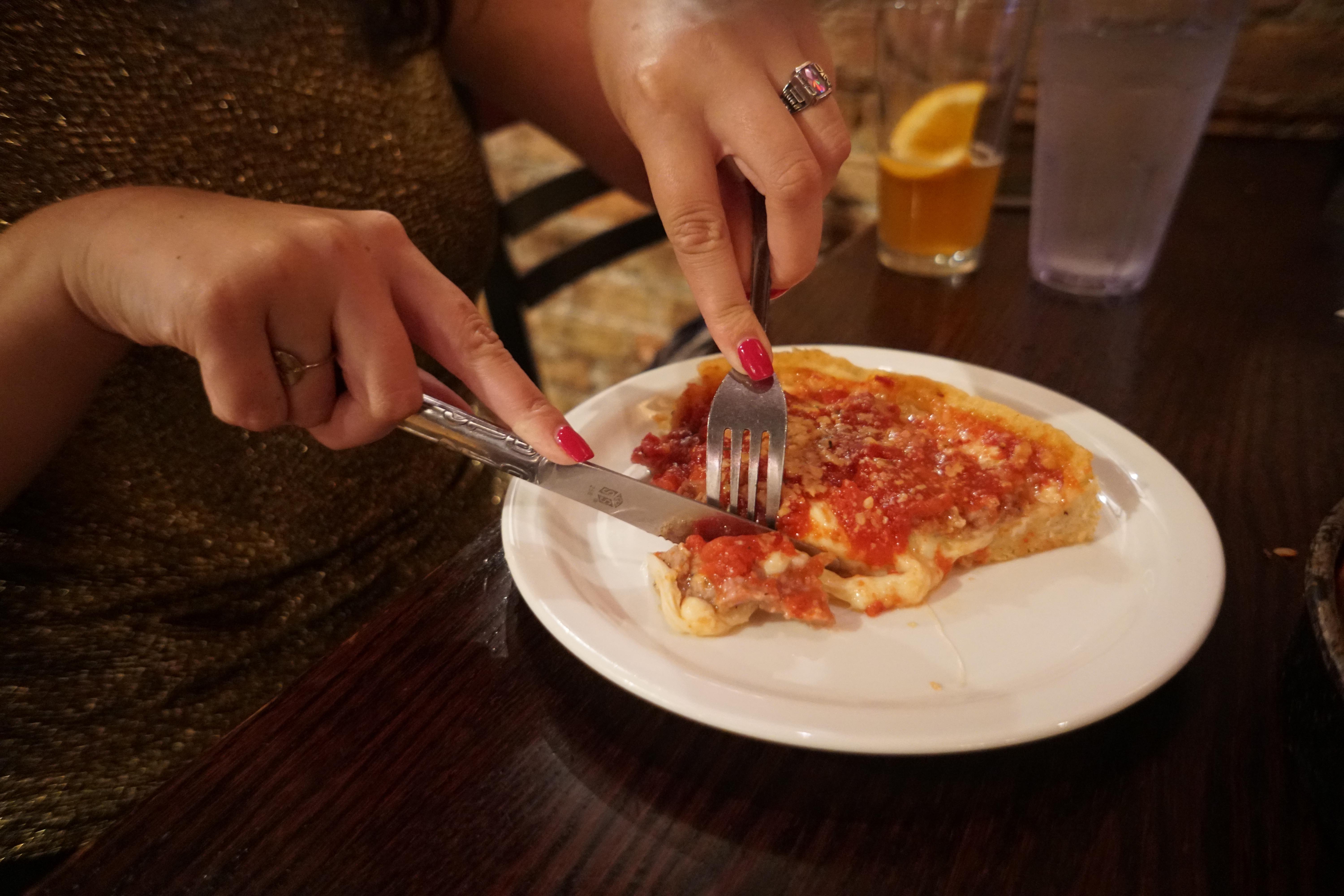 woman with red nails cutting deep dish pizza with a knife and fork
