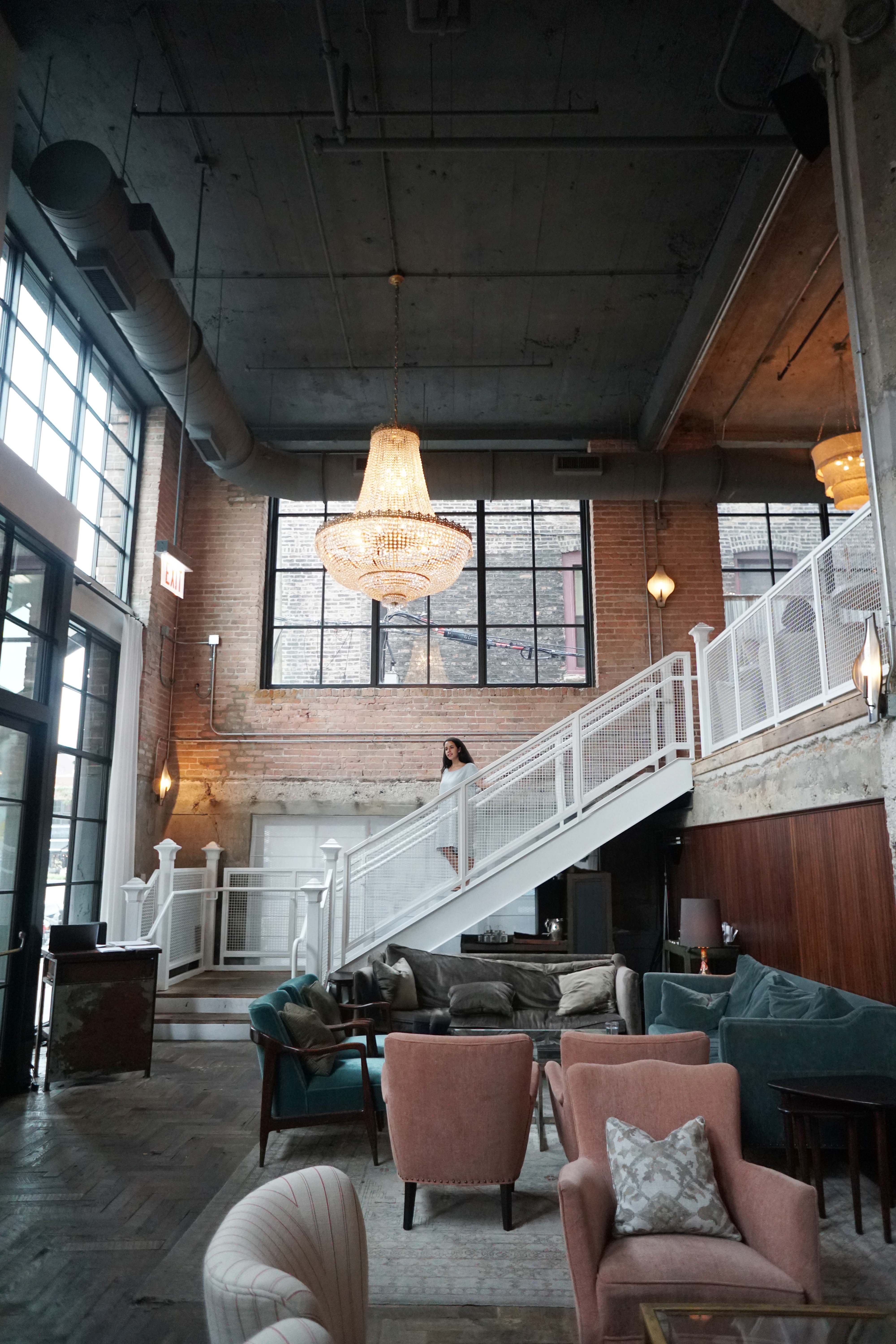 Woman walking down the stairs in entranceway lobby of Soho House Chicago Hotel under chandelier 